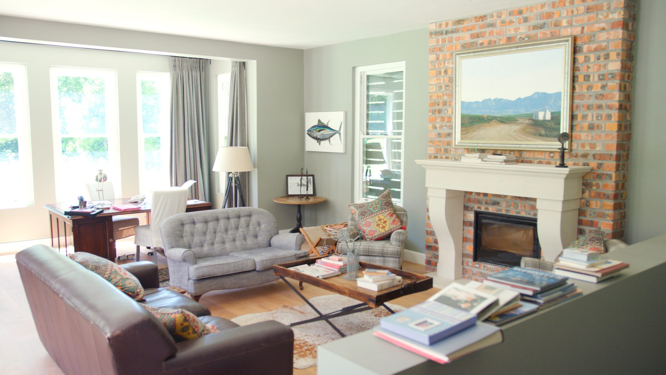 Comfortable American living room with exposed brick fireplace, tufted sofa and landscape painting