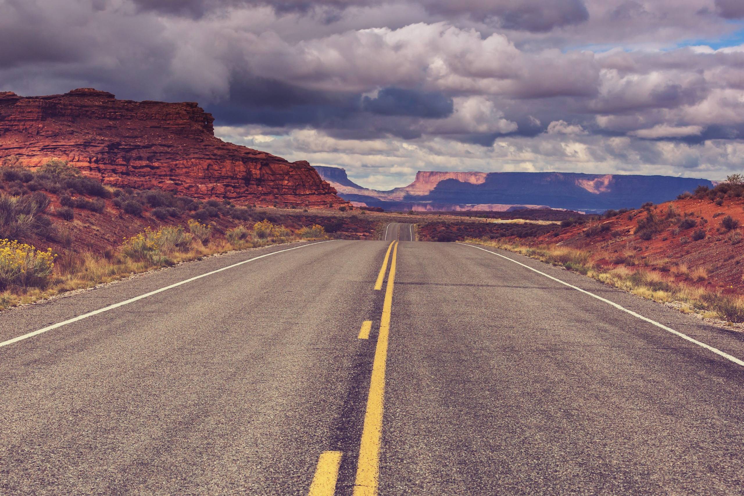 Empty highway through the American Southwest with red mesa formations and dramatic cloudy sky