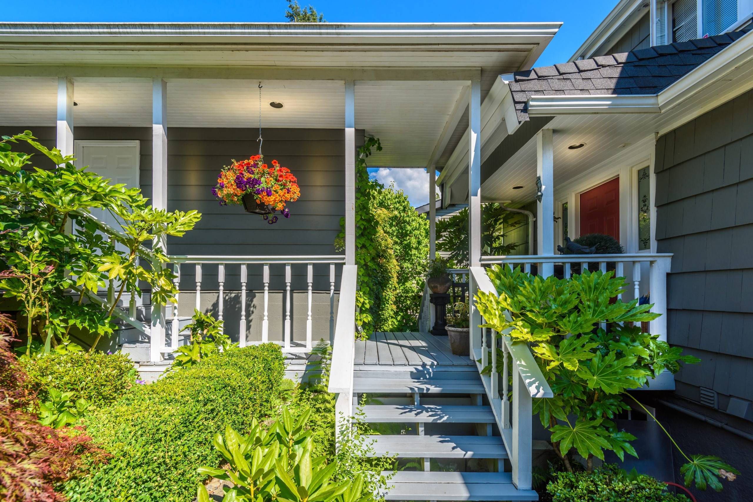 Beautiful American front porch with hanging flower baskets, white chairs and hydrangea garden