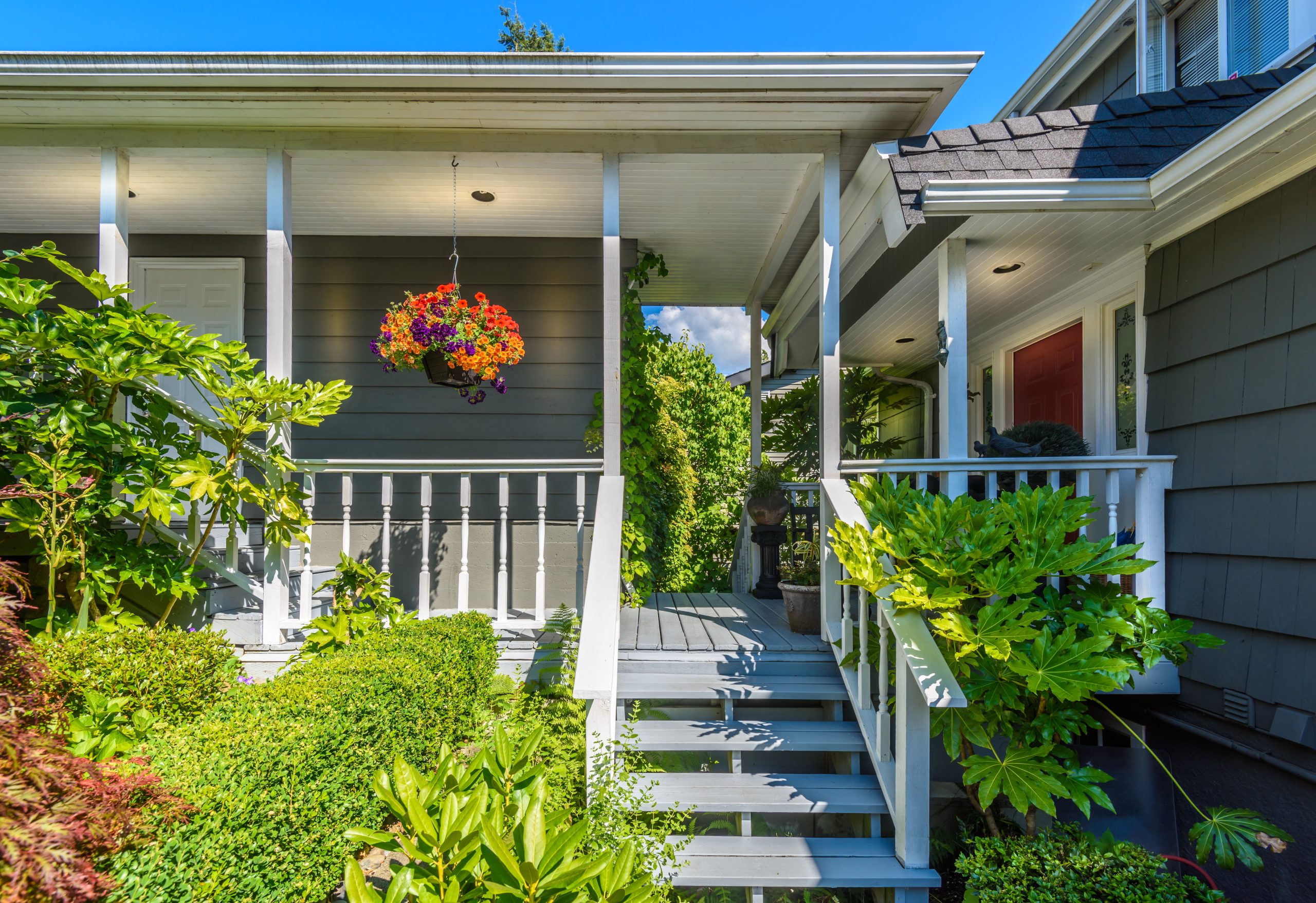 Beautiful American front porch with hanging flower baskets, white chairs and hydrangea garden