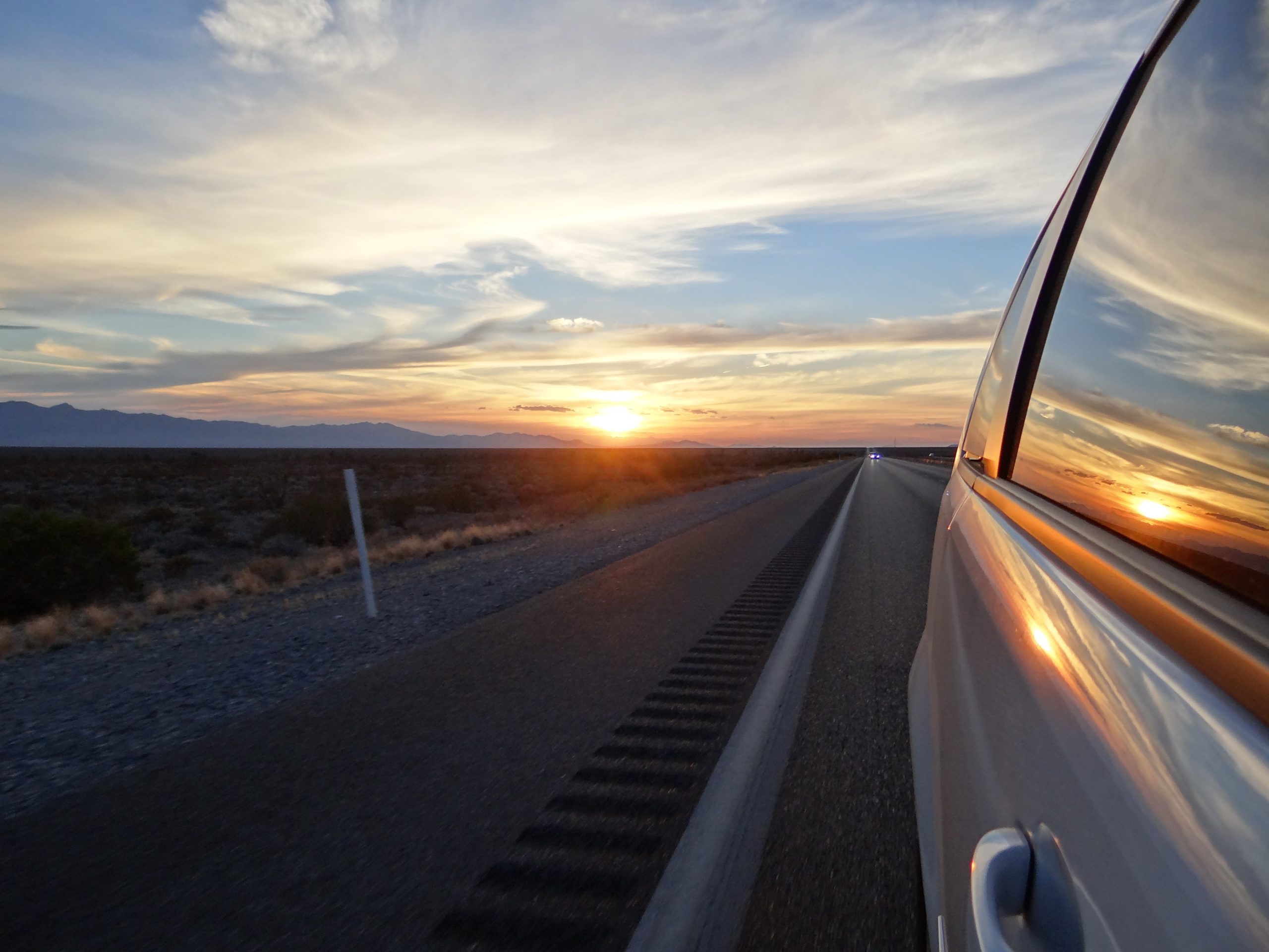 Lone car driving straight desert road in California with telephone poles — American road trip scenery