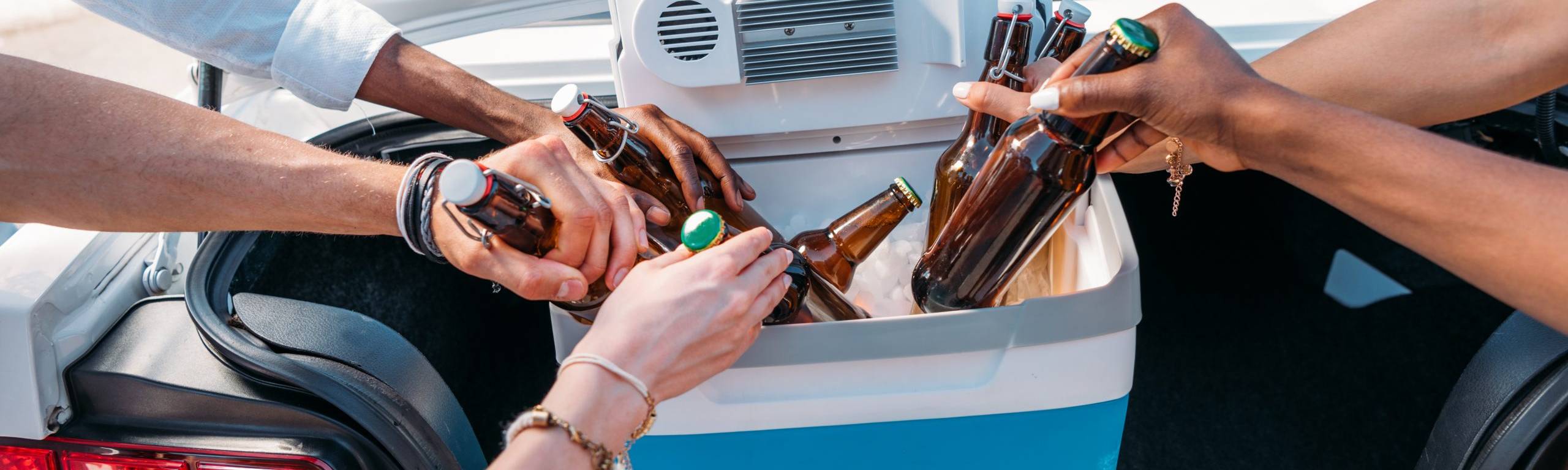 Friends grabbing cold drinks from insulated cooler in car trunk on road trip