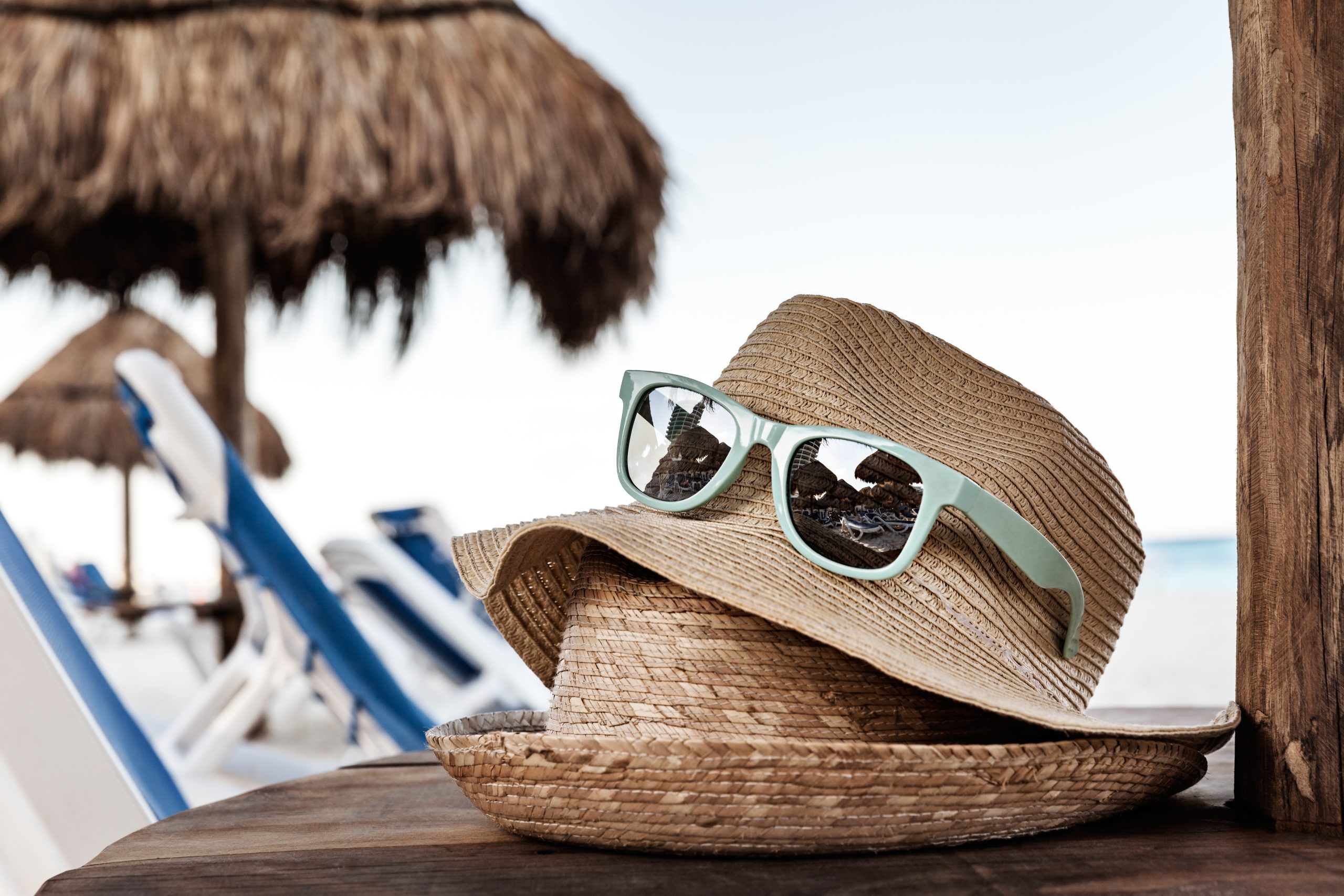 Wide brim sun hat and polarized sunglasses on wooden table at beach — road trip sun protection essentials